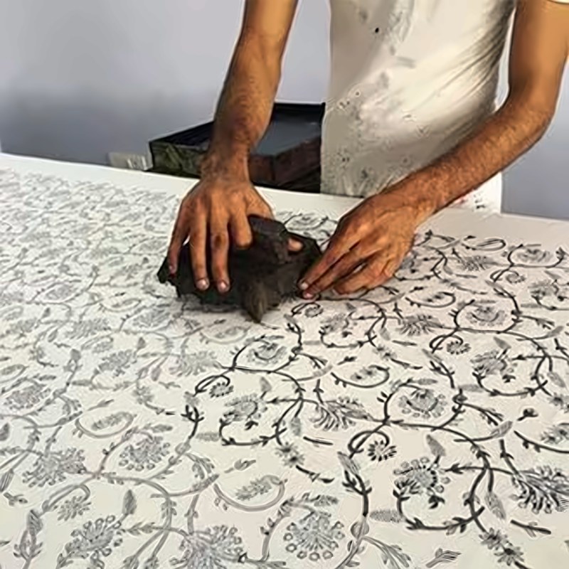 A printer pressing a carved wooden block to stamp a fine floral pattern onto white cotton
