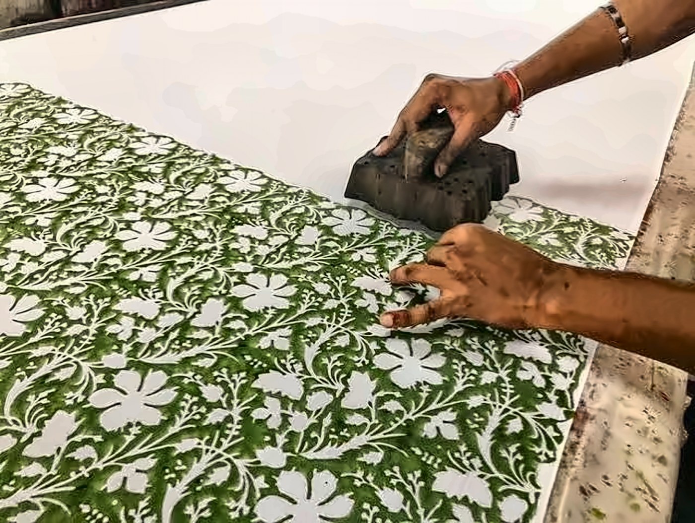 Hands pressing a carved wooden block to print a green floral pattern
